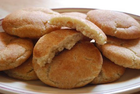 a pile of snickerdoodle cookies on a white plate with one broken in half
